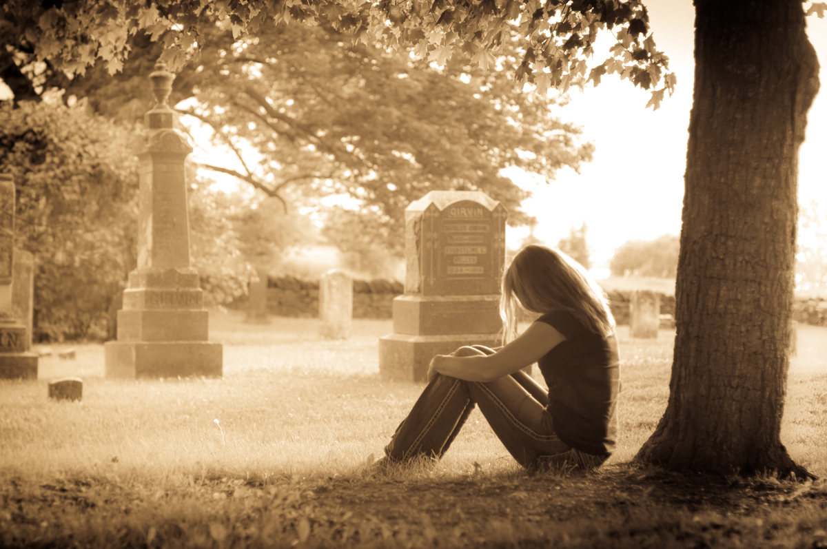 woman-sitting-in-front-of-a-tree-in-a-cemetery-grieving