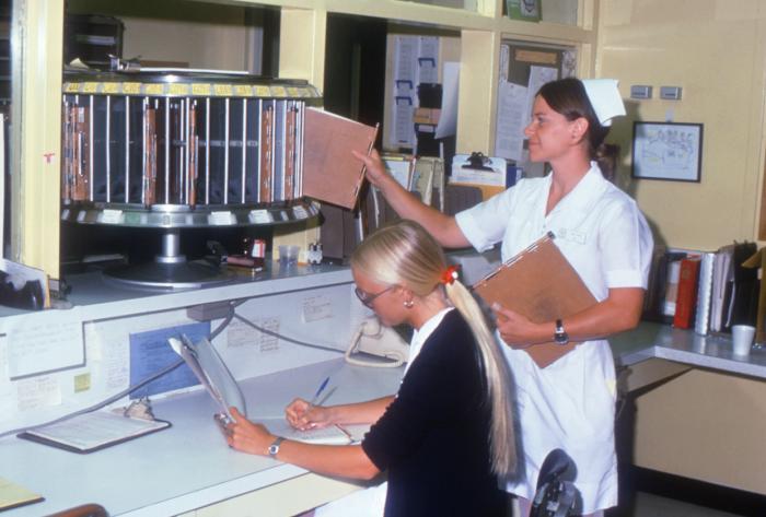 two hospital personnel working with patients' records at a nurse’s station.