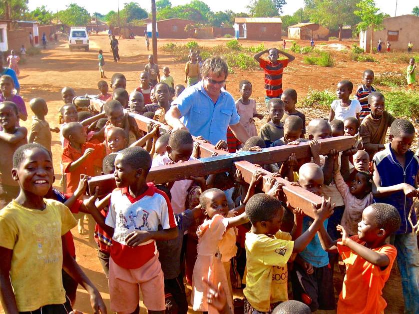 a man surrounded by children, all carrying a large cross
